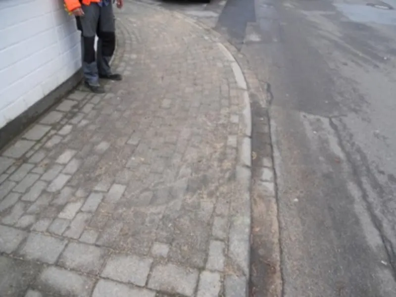 Geschwungener Gehweg aus Kopfsteinpflaster mit angrenzender Straße